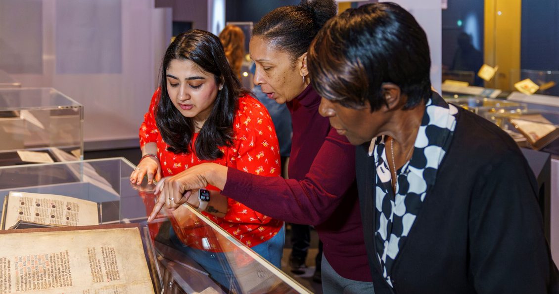 A photo of three people looking at a display cabinet in an exhibition at the British Library