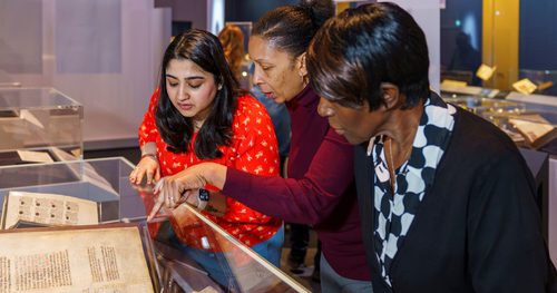 A photo of three people looking at a display cabinet in an exhibition at the British Library