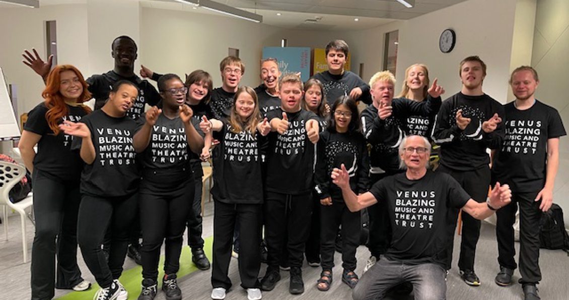 A photograph of a group of performers all wearing black t-shirts with white writing on that says Venus Blazing Music and Theatre Trust