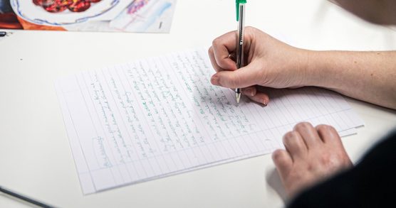 A hand writing with a pen on lined paper