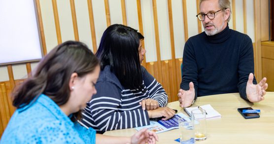 Three people sat at a table in a workshop.
