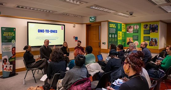 A group of people sitting in chairs looking towards workshops leaders who sit in front of a large screen