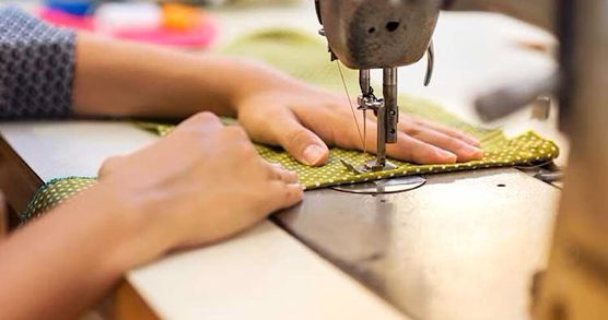 A piece of green fabric is being run through a sewing machine