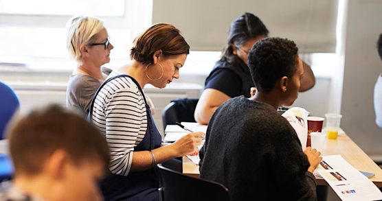 A group of adults seated around a desk looking attentively at sheets of paper in front of them