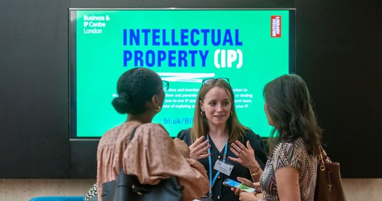 Three women talking at the BIPC with Intellectual Property digital display in background.