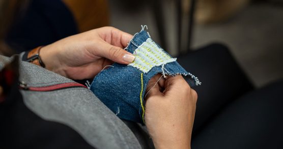 Photograph of hands holding a needle and thread stitching on a blue fabric.
