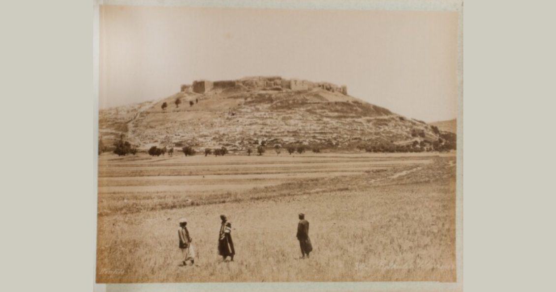 Archival sepia-toned photo depicting three people standing within Palestinian landscape with the city of Jericho in the background