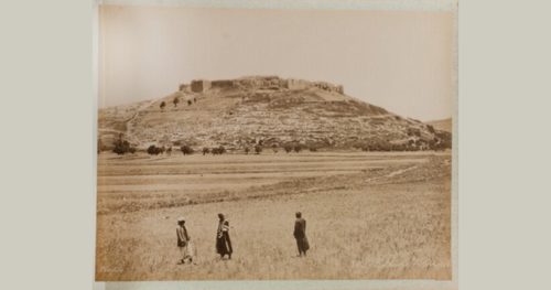 Archival sepia-toned photo depicting three people standing within Palestinian landscape with the city of Jericho in the background