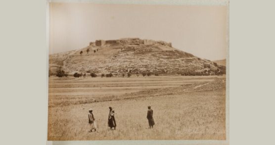 Archival sepia-toned photo depicting three people standing within Palestinian landscape with the city of Jericho in the background