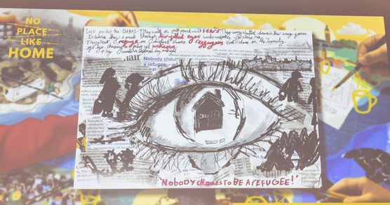 A black and white artwork projected on a screen, featuring a large eye, with a house where the pupil should be, and the wording 'Nobody chooses to be a refugee!'
