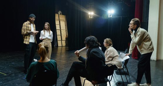 A group of theatre practitioners sit on a black stage in deep discussion.
