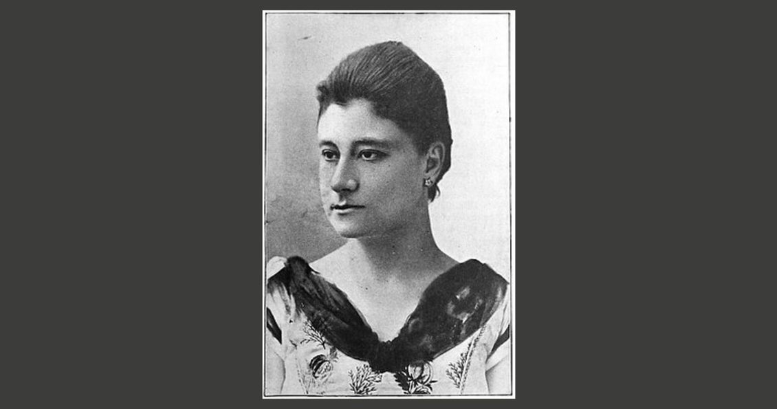 Head and shoulders photo of a woman wearing a decorative dress and small earrings.