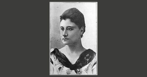 Head and shoulders photo of a woman wearing a decorative dress and small earrings.