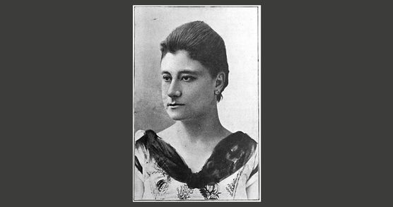 Head and shoulders photo of a woman wearing a decorative dress and small earrings.