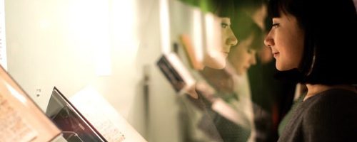 A woman wearing a dark top and hair in a bob looks at a display case of open books