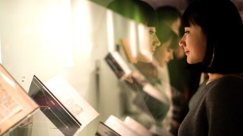 A woman wearing a dark top and hair in a bob looks at a display case of open books