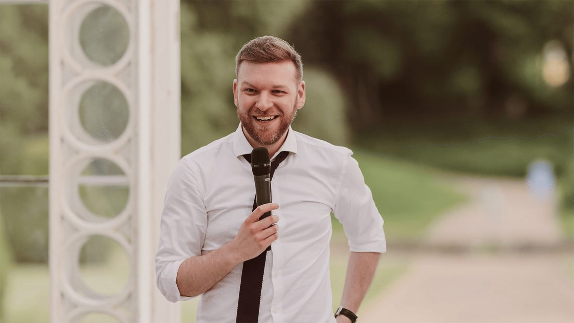 Photo of Andrew Gear in a white shirt holding a microphone.