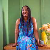 Wendy smiling, wearing a blue dress, and sitting on a counter against a panelled wall.