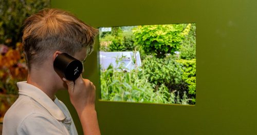 A school child holding a speaker to their ear while looking at a screen showing the tops of green trees
