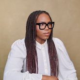A woman with long braided hair wearing a white shirt and square glasses with thick, black frames