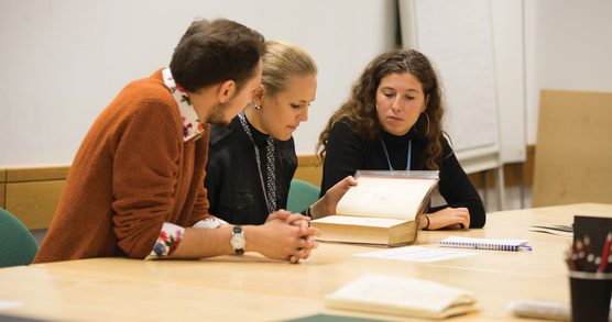 Three researchers at a desk examining a book together.
