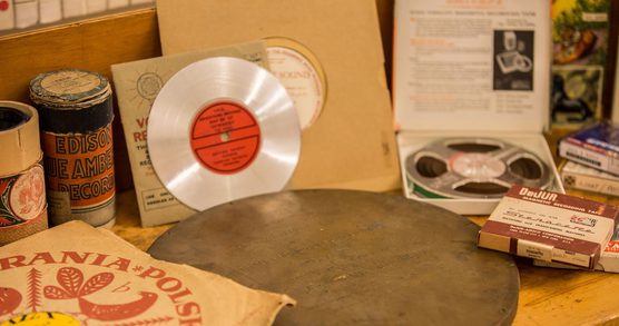 Various archival items and equipment relating to the recording of sound and music including a CD, vinyl in paper sleeves and wax cylinder tubes.