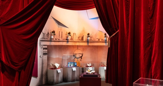 Plush red velvet curtains are pulled open to reveal a fairy tale fireplace and six books in cases