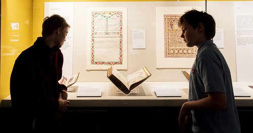 A silhouette of two school children looking into a backlit display case of manuscripts