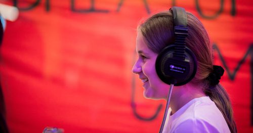 A school age child in a wearing headphones against a red background