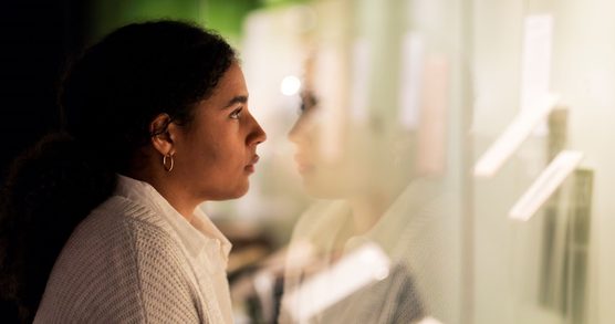 A school age student wearing a shirt and a beige cardigan stands in front of an exhibition display case and gazes into it