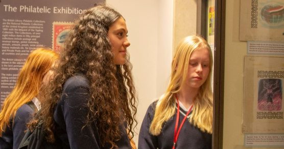 Three school age students wearing school uniforms with long hair, worn loose, are looking at a display of stamps