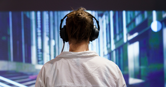 A person, seen from behind, wearing a white shirt, headphones and hair in a bun. They are looking at a blue patterned image