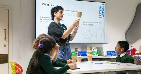 Chloe is facilitating our Sounds Lab workshop. She is holding a paper cup and a pencil, and she is explaining how to amplifying sound.