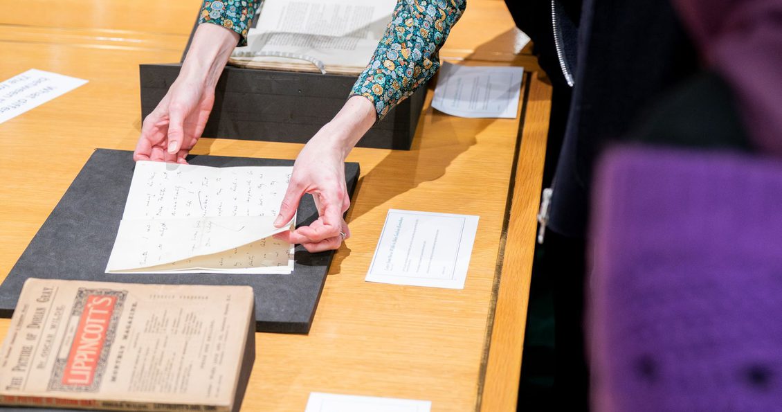 A woman shows Library collection items to two people. One is wearing a purple head scarf