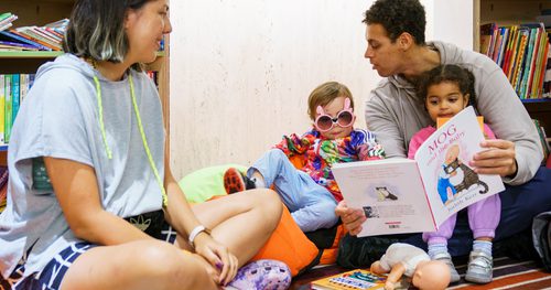 A family with two adults and two children sat on the floor reading some children's books
