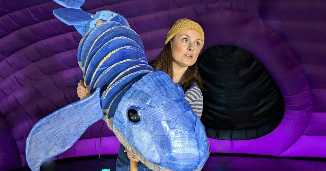 An adult holding a puppet of a blue whale