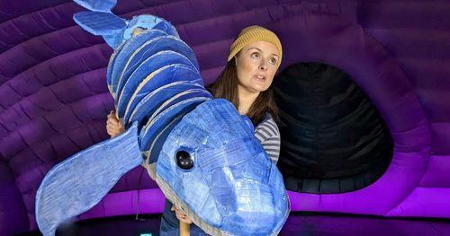 An adult holding a puppet of a blue whale