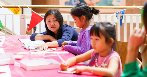 Mother and daughter engaging with activity while another girl draws.