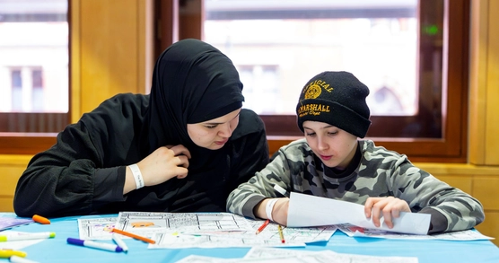 An adult and child sit together at a table of craft materials