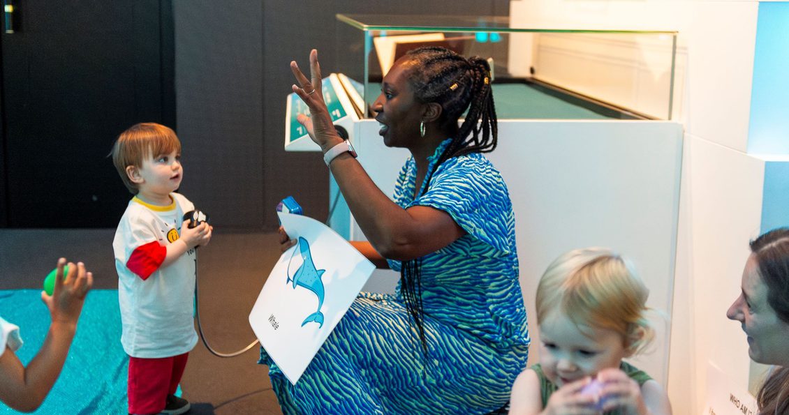 Wendy raising her arm as she tells a story to toddlers.