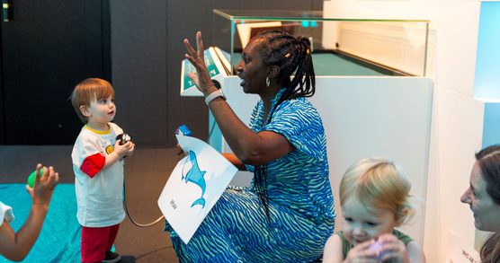Wendy raising her arm as she tells a story to toddlers.