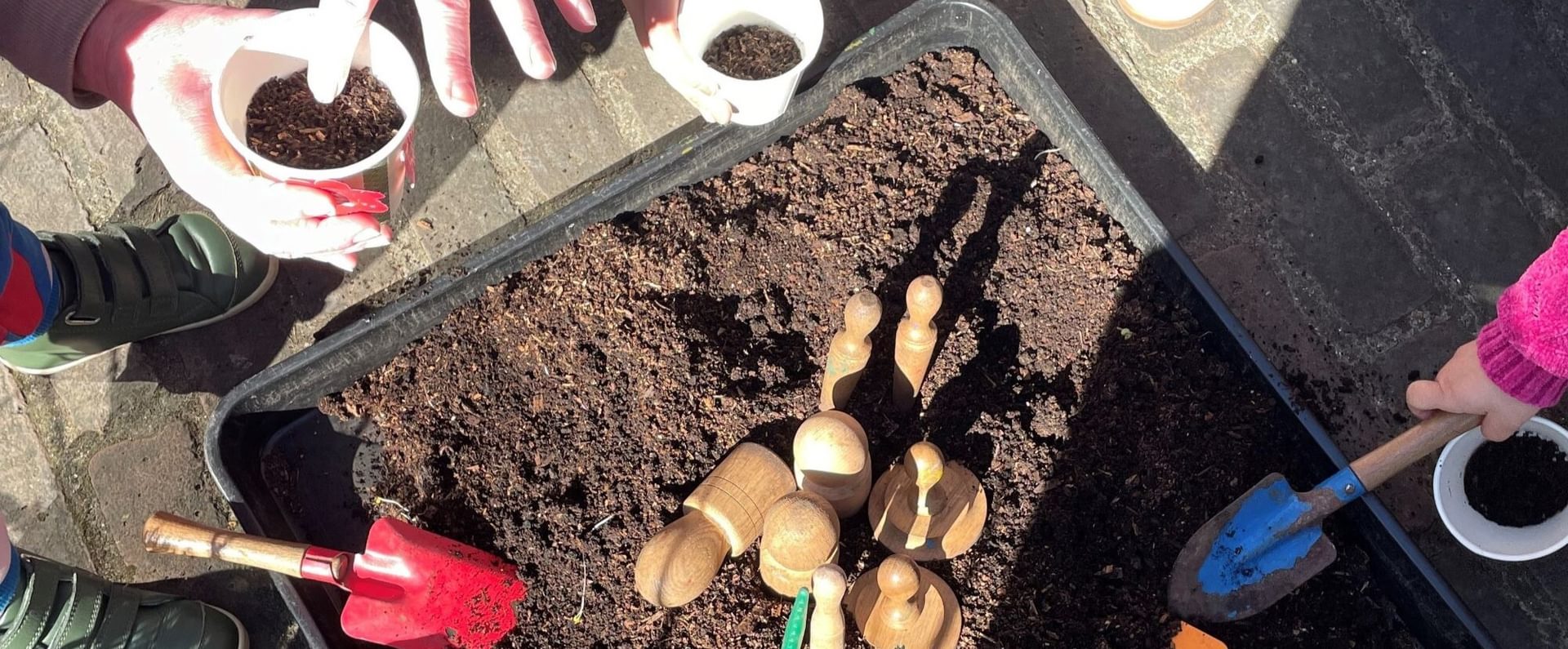 Hands of a child and an adult over a planter, planting seeds in the soil.