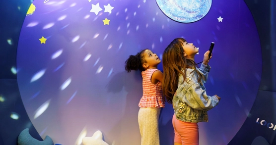 Two children in a space-themes room looking up to the sky. One is holding a torch.