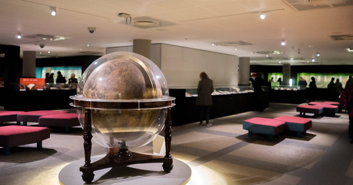 A spot-lit large globe set into a wooden frame standing on a low pedestal in an exhibition gallery